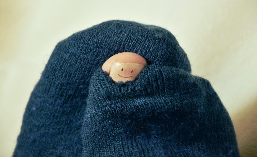 A finger with a smiling face drawn on the nail sticking out of a hole in a sock