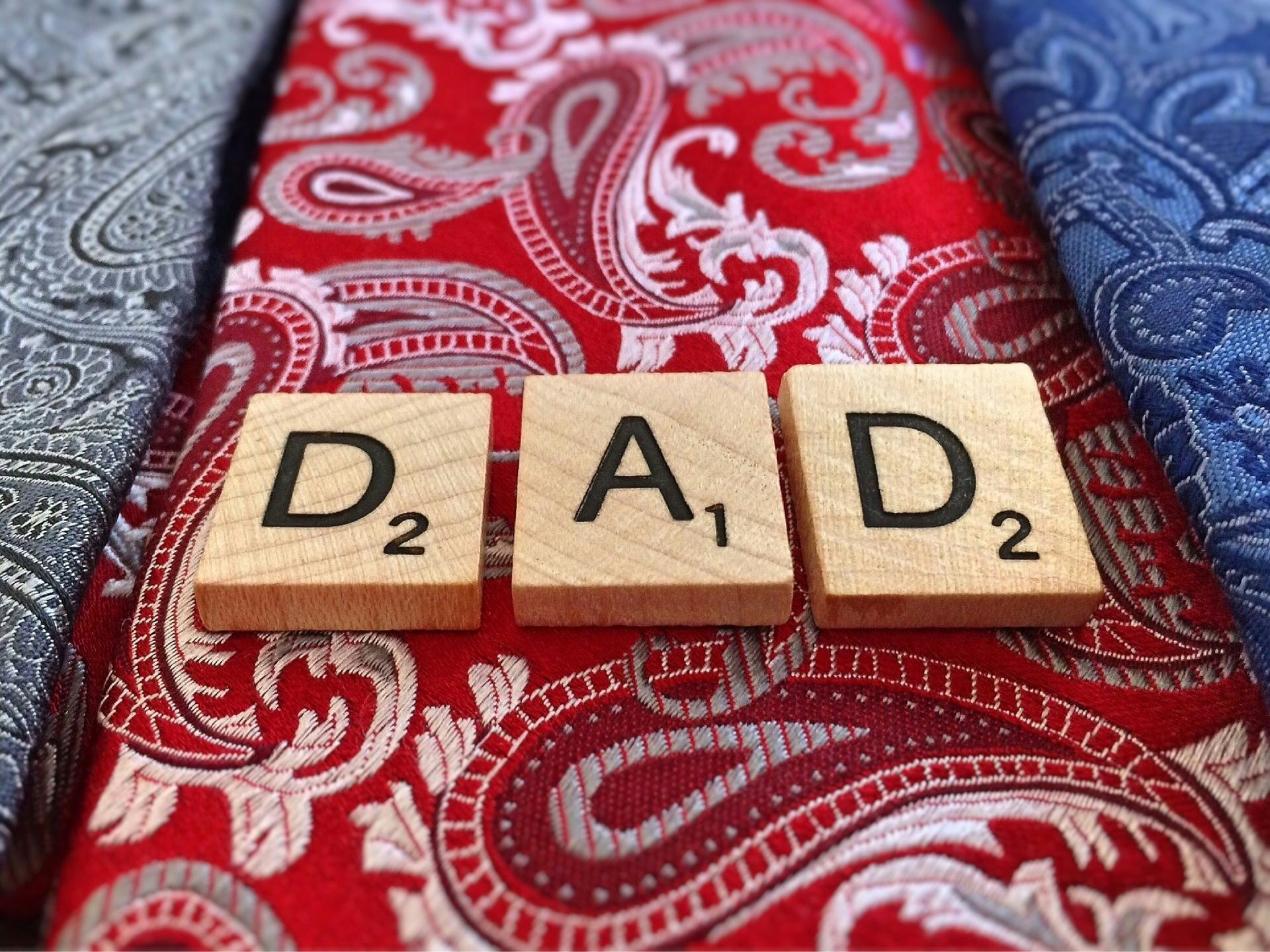 Three wooden scrabble elements forming the word 'DAD' on a red tie