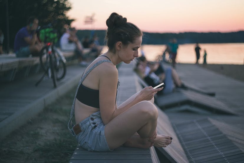 A woman sitting alone on her phone at a beach next to the sea