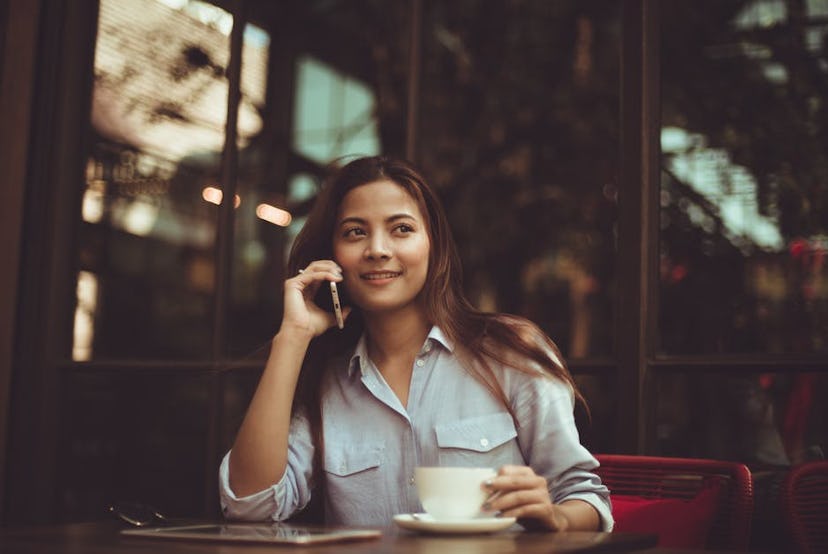 Young lady talking on a phone while drinking coffee in a bar