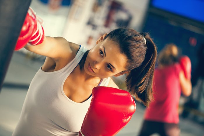 A woman wearing a white tank top and boxing gloves hits a punching bag