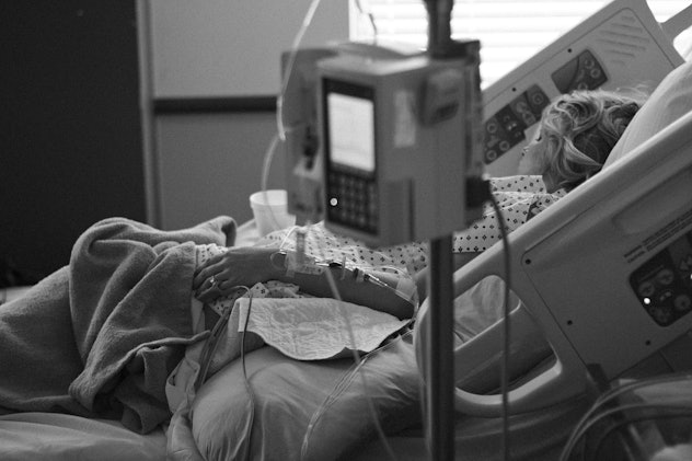 A black and white photo of a pregnant woman lying in the hospital bed. 