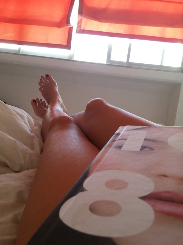 Woman lying in bed with the book on her bare legs.