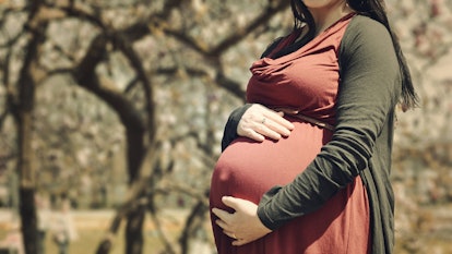 A pregnant woman standing outside with her hand on her stomach