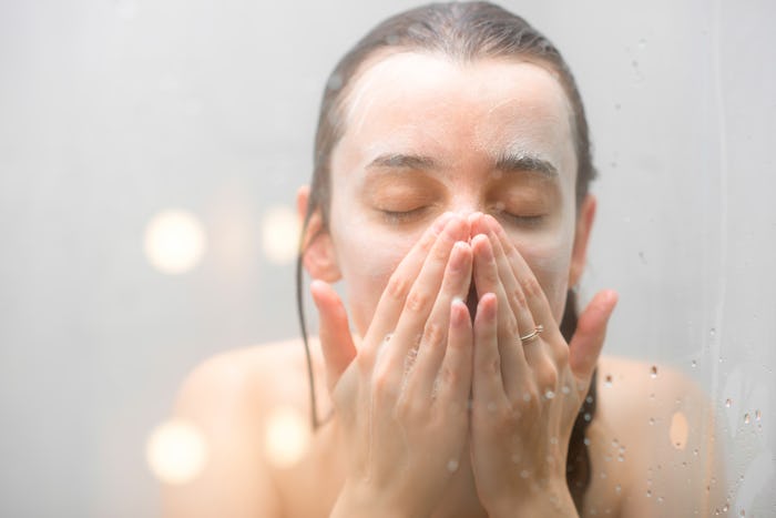 A woman in a shower washing her face and making some of the surprising hygiene mistakes that cause a...