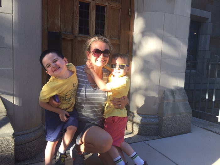 Woman holding her two kids in front of a building on a sunny day