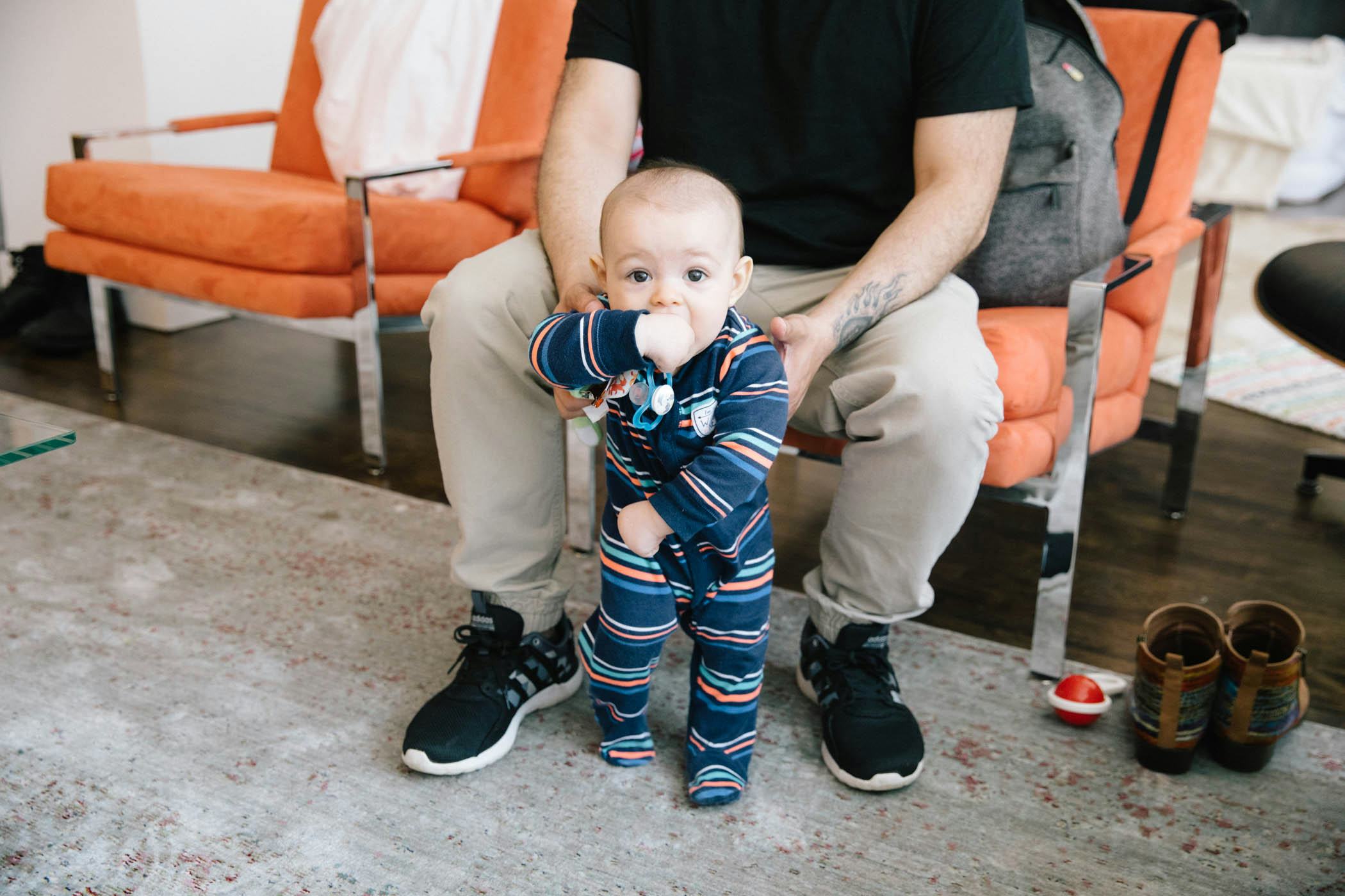 Dad sitting in a chair while holding his baby who is trying to walk 