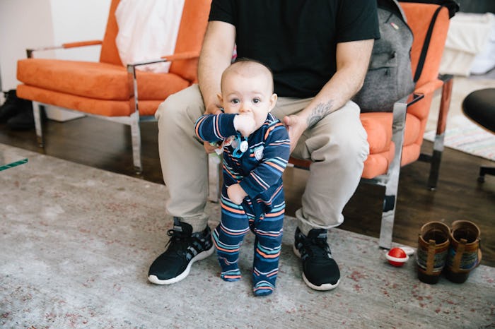 Dad sitting in a chair while holding his baby who is trying to walk