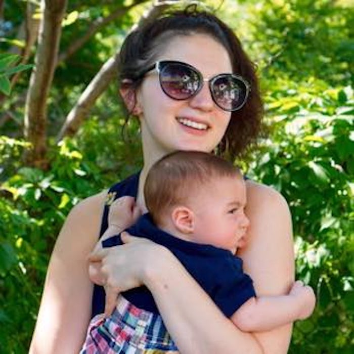 Cooper Fleishman wearing dark shades, smiling while holding her newborn baby with trees in the backg...