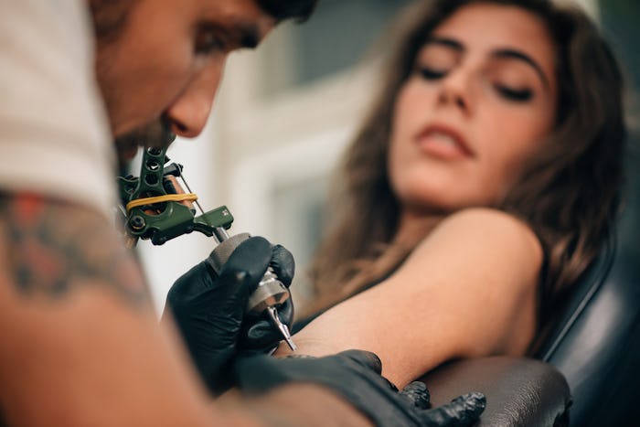 A young lady getting a tattoo on her left hand