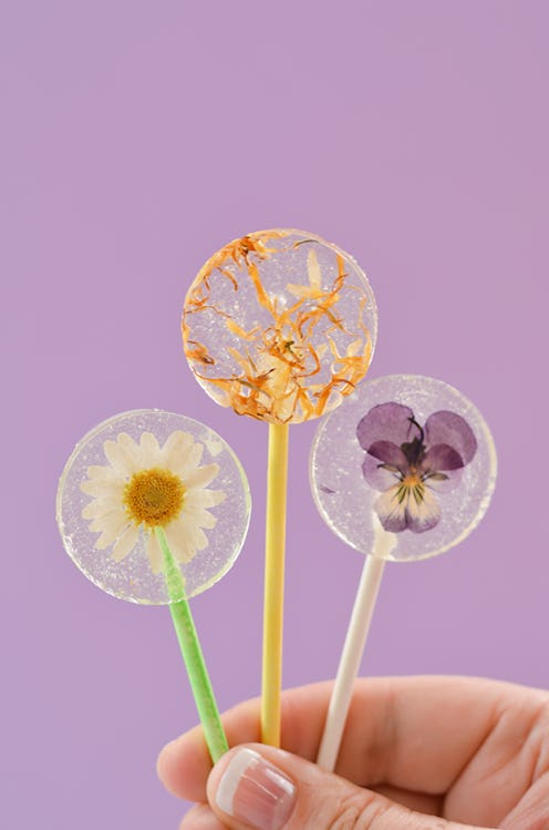 A hand holding three DIY lollipops with violet, daisy and dandelion inside made for National Lollipo...