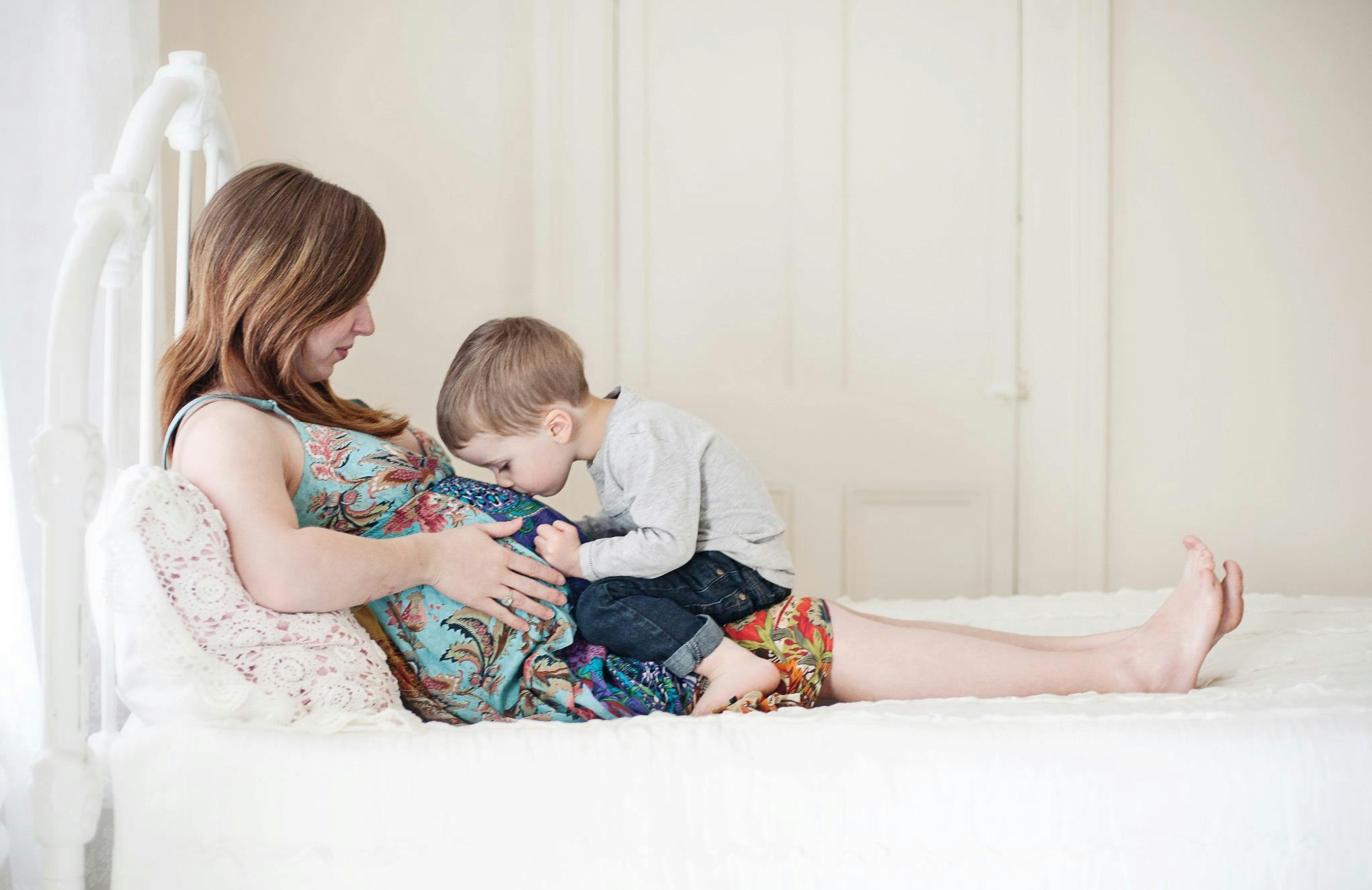 A pregnant woman lying on her bed and her son kissing her stomach