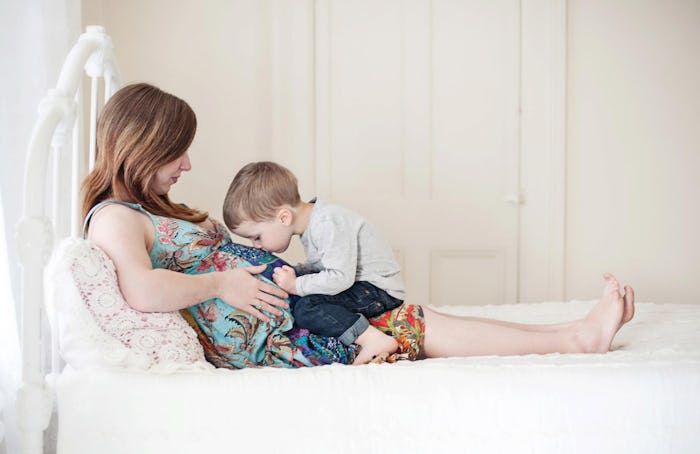 A pregnant woman lying on her bed and her son kissing her stomach