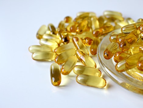 Yellow semi-translucent vitamins in pill form on a glass bowl and spilled around it