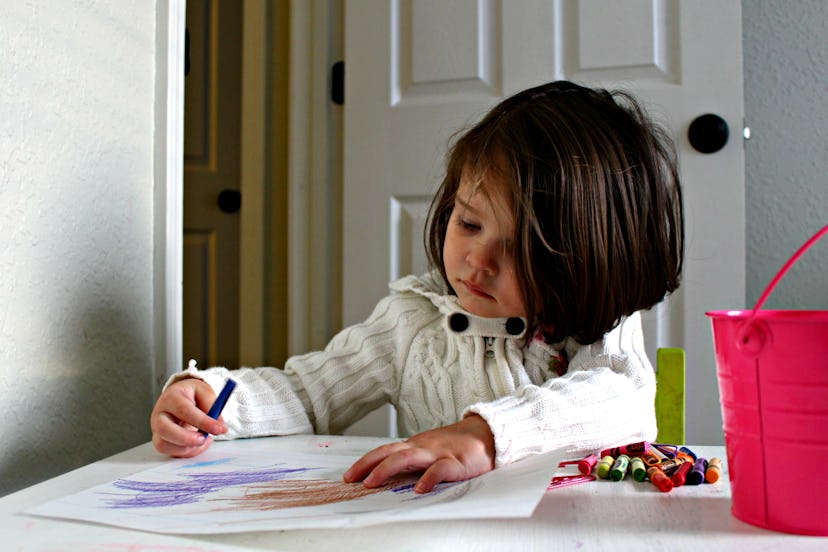 A little girl using her crayons to draw on paper