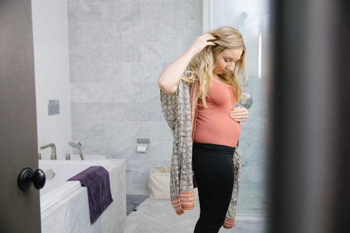 A pregnant woman standing in the bathroom feeling her belly