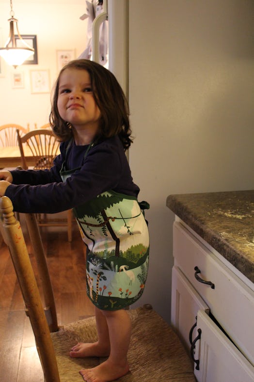 A child standing on the chair in the kitchen, helping her mom cook