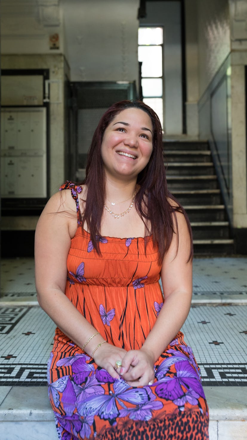 A woman sitting on a tiled floor in front of a staircase wearing a floral orange and purple sundress