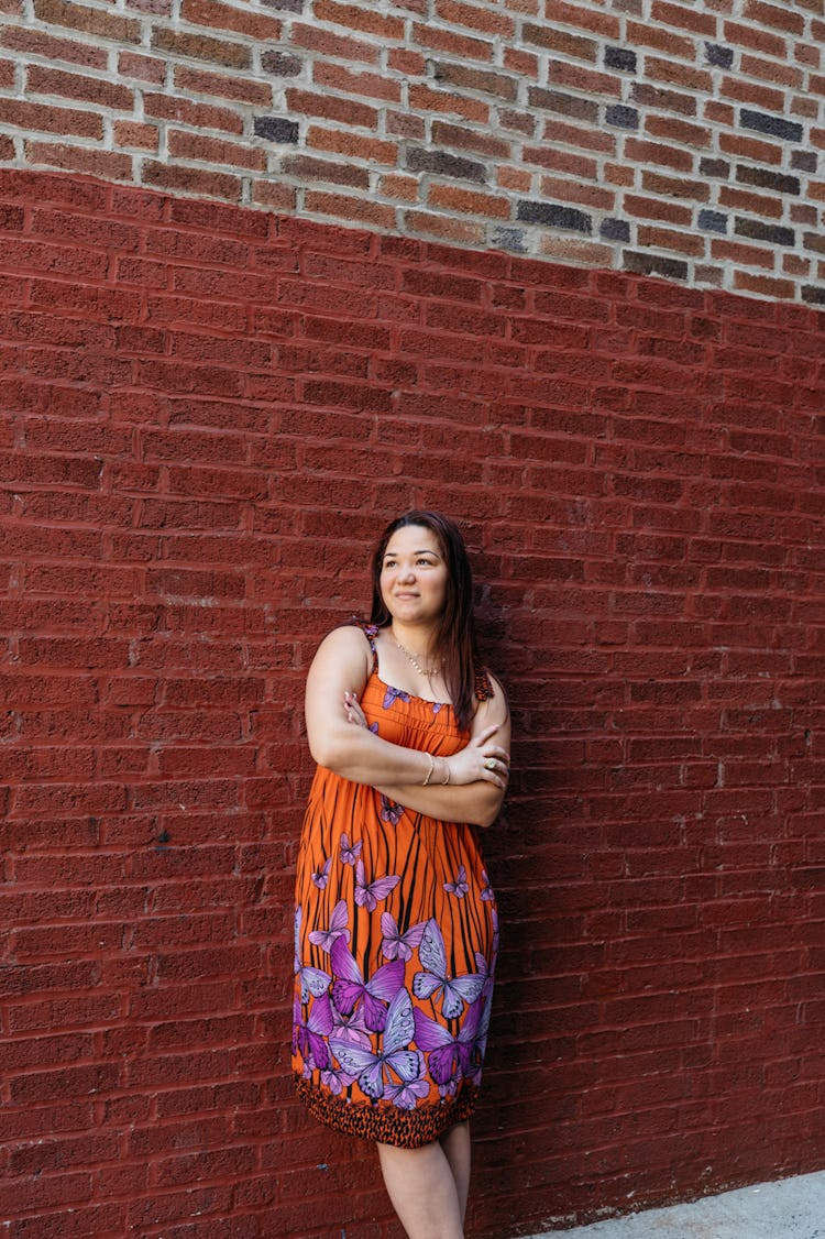  Ashley Batz stands in front of a brick wall in a colorful dress