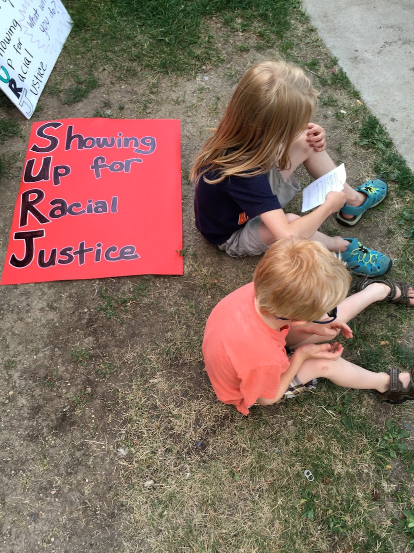 Two kids sitting on ground next to a red poster with black "showing up for racial justice" text