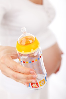 A pregnant woman holding an empty baby bottle