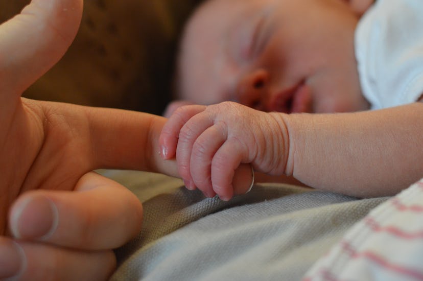 A newborn holding mother's finger while sleeping