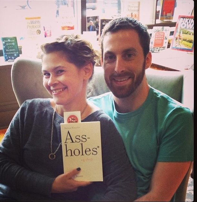 A woman sitting next to her partner and holding the 'Ass-holes' book