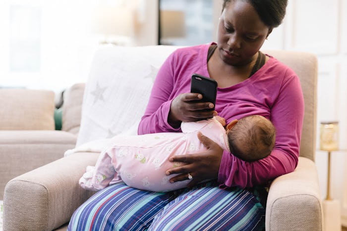 A mother breastfeeding her newborn baby while looking at her phone