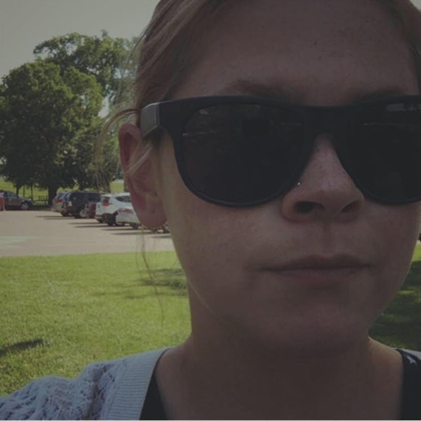 A woman wearing dark shades with a park in her background