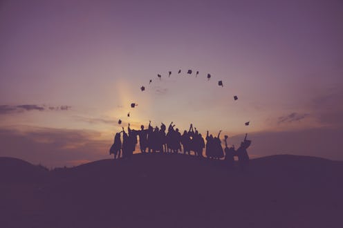 Silhouettes of college grads throwing their graduation hats in the air on top of a hill during the s...