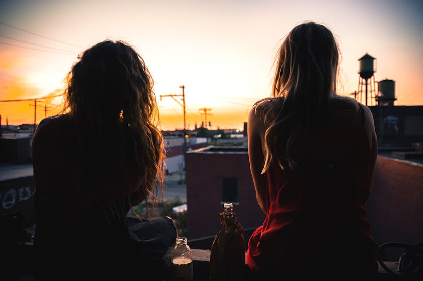 Two girl friends sitting on a rooftop, enjoying sunset