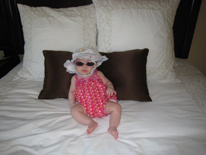 Crystal Henry's baby wearing a hat and sunglasses while lying on the bed