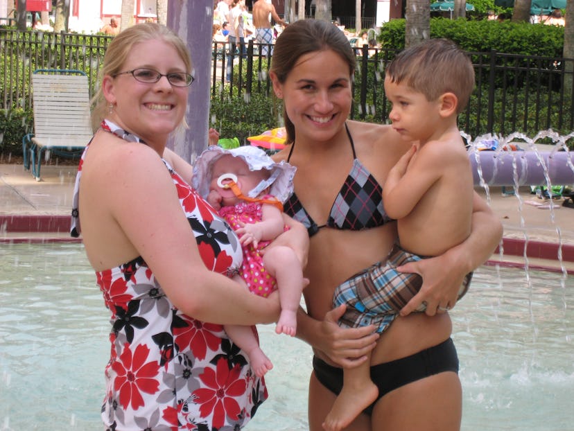 Crystal Henry wearing a one-piece bathing suit while holding her baby next to her friend holding her...