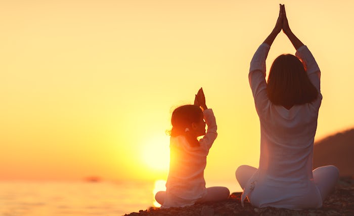 A mother doing yoga with her daughter as a part of 'Enlightened Parenting' while watching a sunset