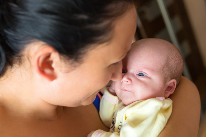 A mother holding her newborn baby wearing a yellow onesie