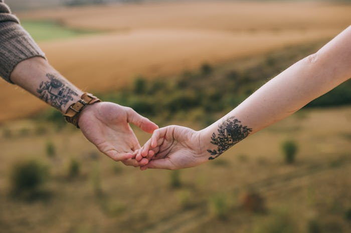 A couple holding hands with matching tattoos on their wrists in front of a beautiful landscape