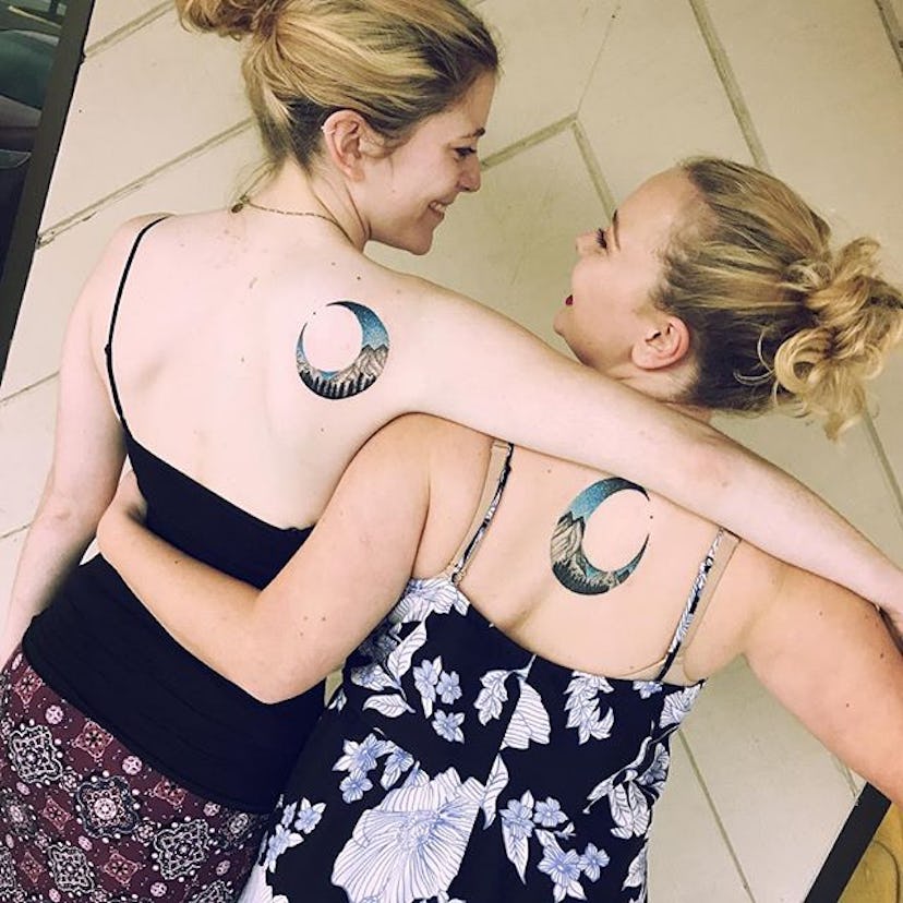 Two women with matching Moon And Mountain tattoos on their back