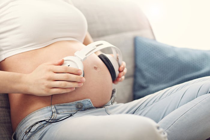 A pregnant woman holding a pair of headphones up to her belly