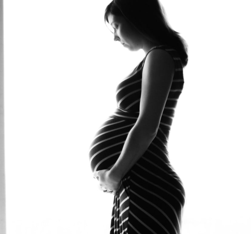 A pregnant woman standing in a black dress and holding her stomach 