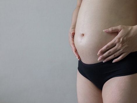 Pregnant woman in underwear  massaging her tummy