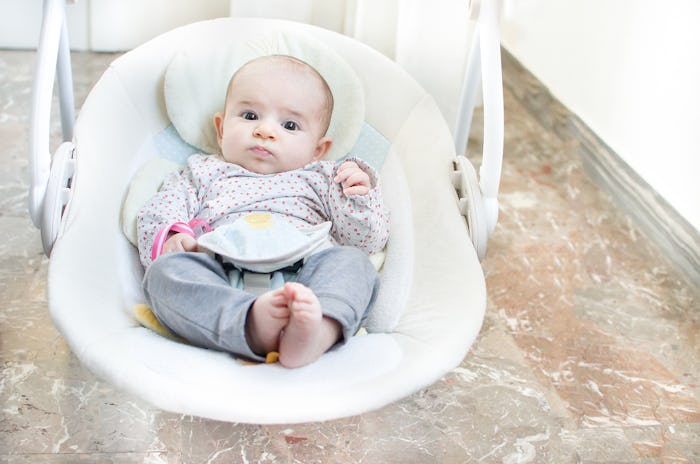 A baby in a white baby swing to help it fall asleep