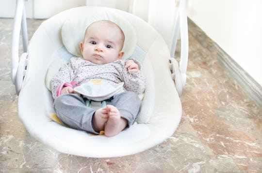 A baby in a white baby swing to help it fall asleep 