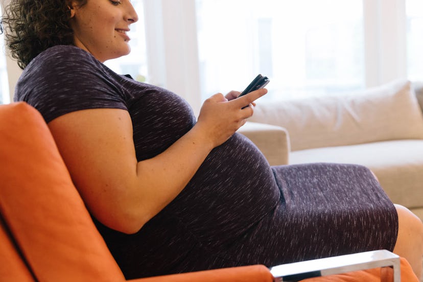 A pregnant woman sitting on a chair and looking into her phone