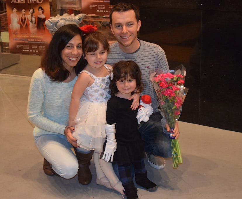 A dad holding the flowers posing for the picture with his wife and two daughters