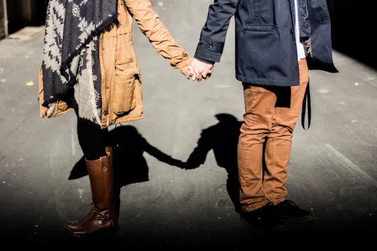A couple standing outside on a autumn day faceing away from each other while holding hands