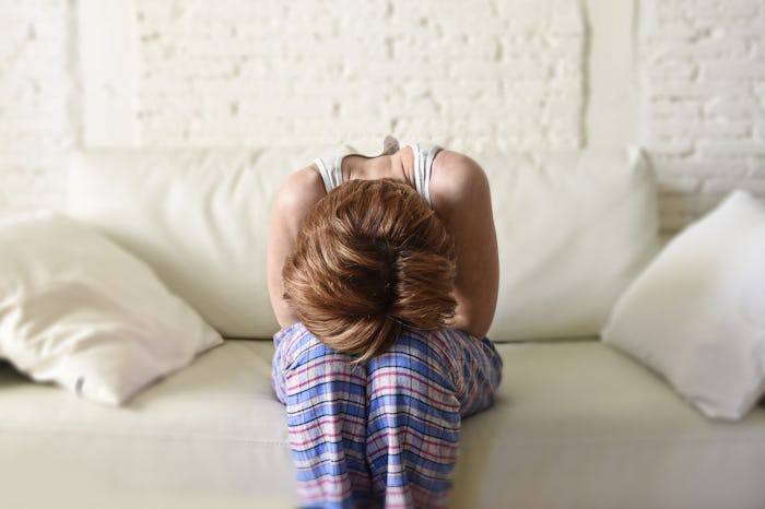 A pregnant woman with pain in her stomach sitting on a couch during her period
