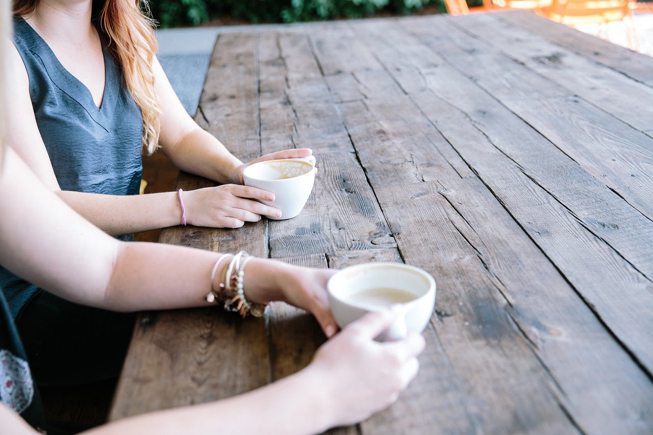 Two ladies are sitting outside at a table and drinking coffee