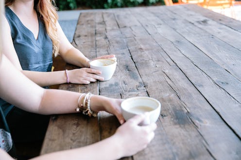 Two ladies are sitting outside at a table and drinking coffee