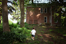 A toddler walking around the front yard of an old house