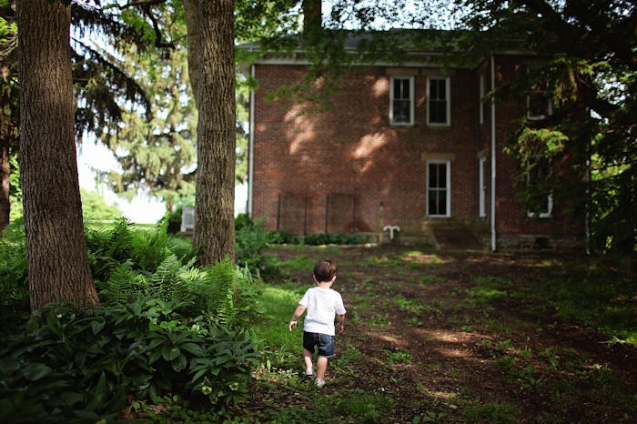 A toddler walking around the front yard of an old house